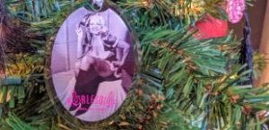 Close-up of ornament featuring b/w photo of Jennie Lee in Santa's helper outfit, hanging on a lit Christmas tree