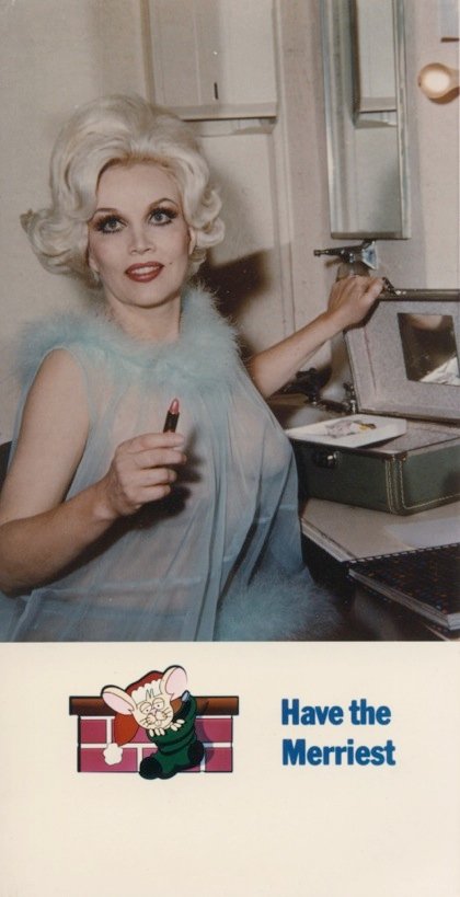 Photo of Liz Renay on her custom holiday card. Below a mouse peeking from a wrapped present says "Have the Merriest"